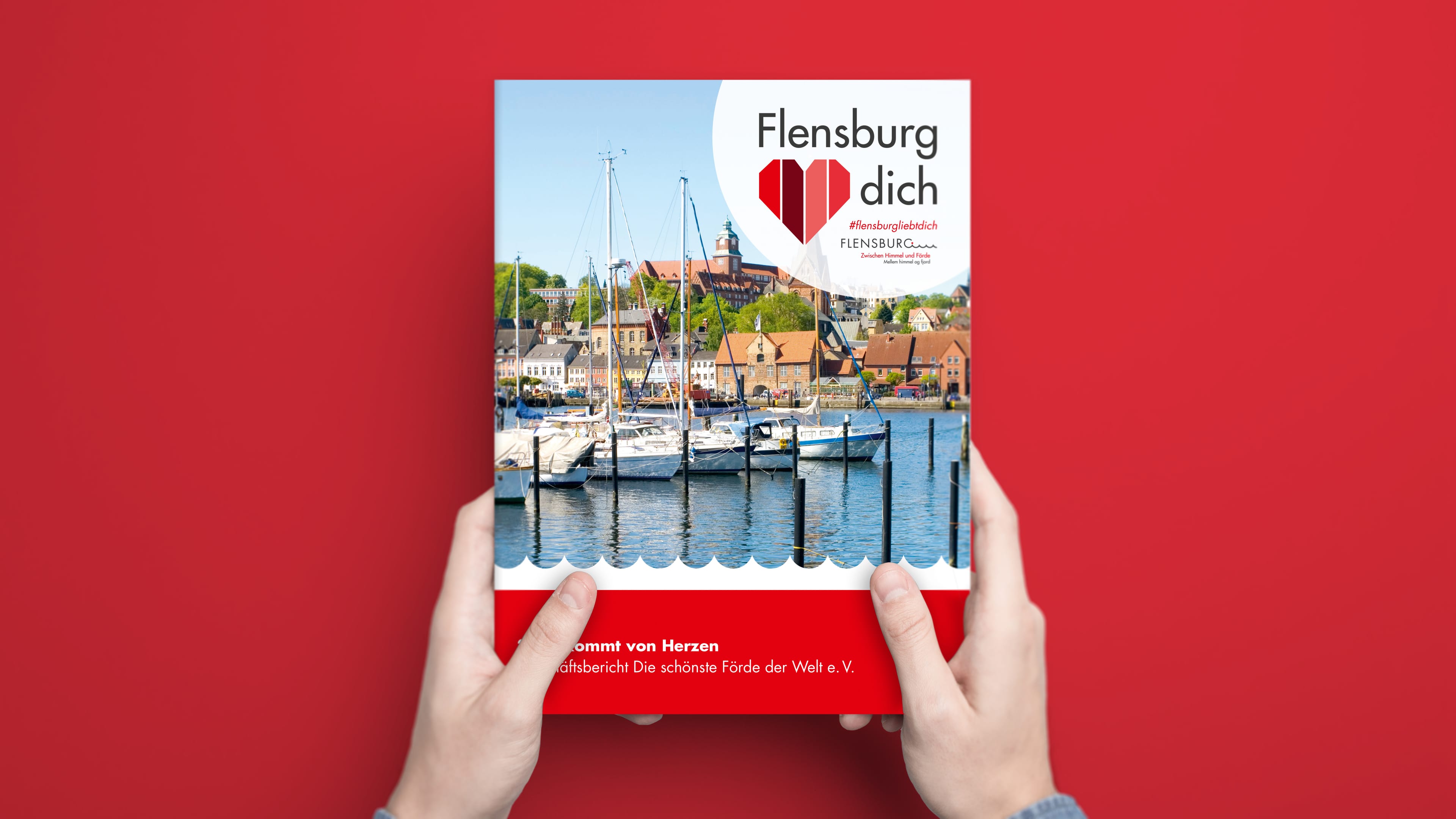 Zwei Hände halten Geschäftsberichte von "Flensburg liebt dich" vor rotem Hintergrund