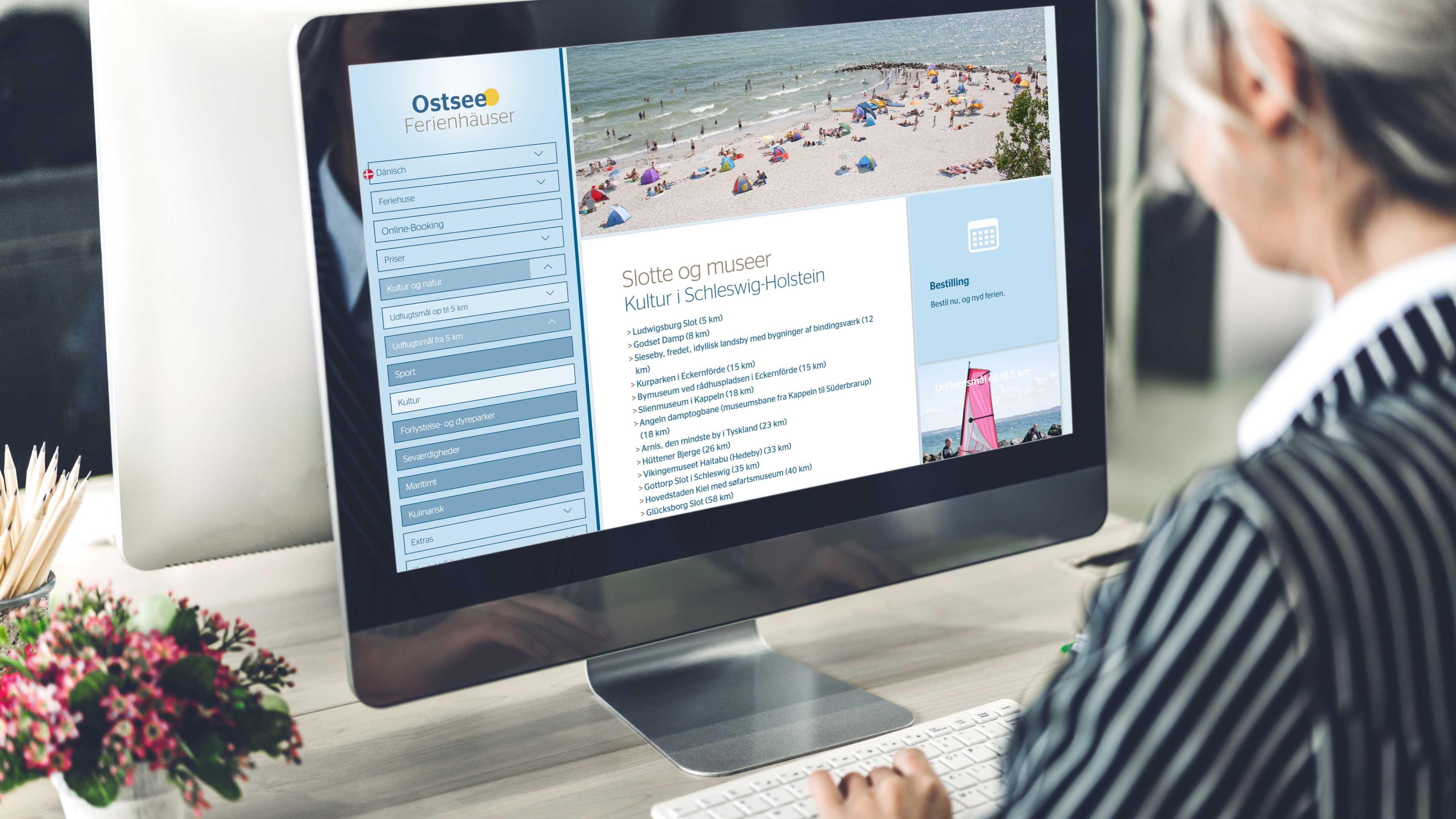 Person sitzt am iMac, das die Website der Ostsee Ferienhäuser zeigt