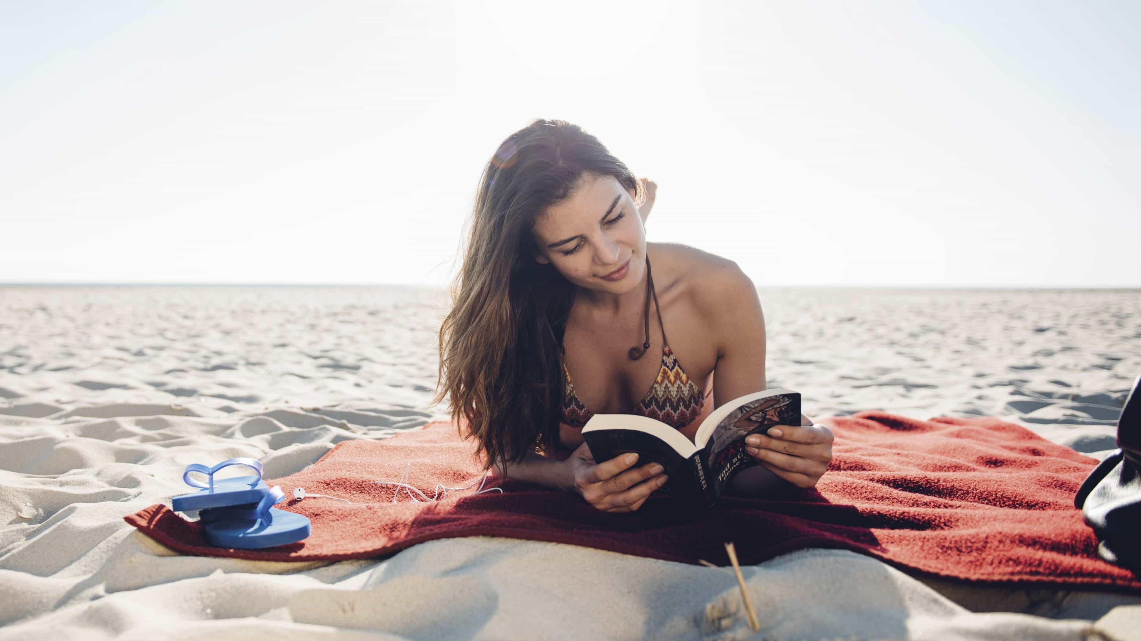 Eine brünette Frau sonnt sich am Strand und leist ein Buch