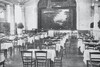 Alte schwarz-weiß Aufnahme eines Festsaals mit Tischen an den jeweils vier Holzstühle stehen