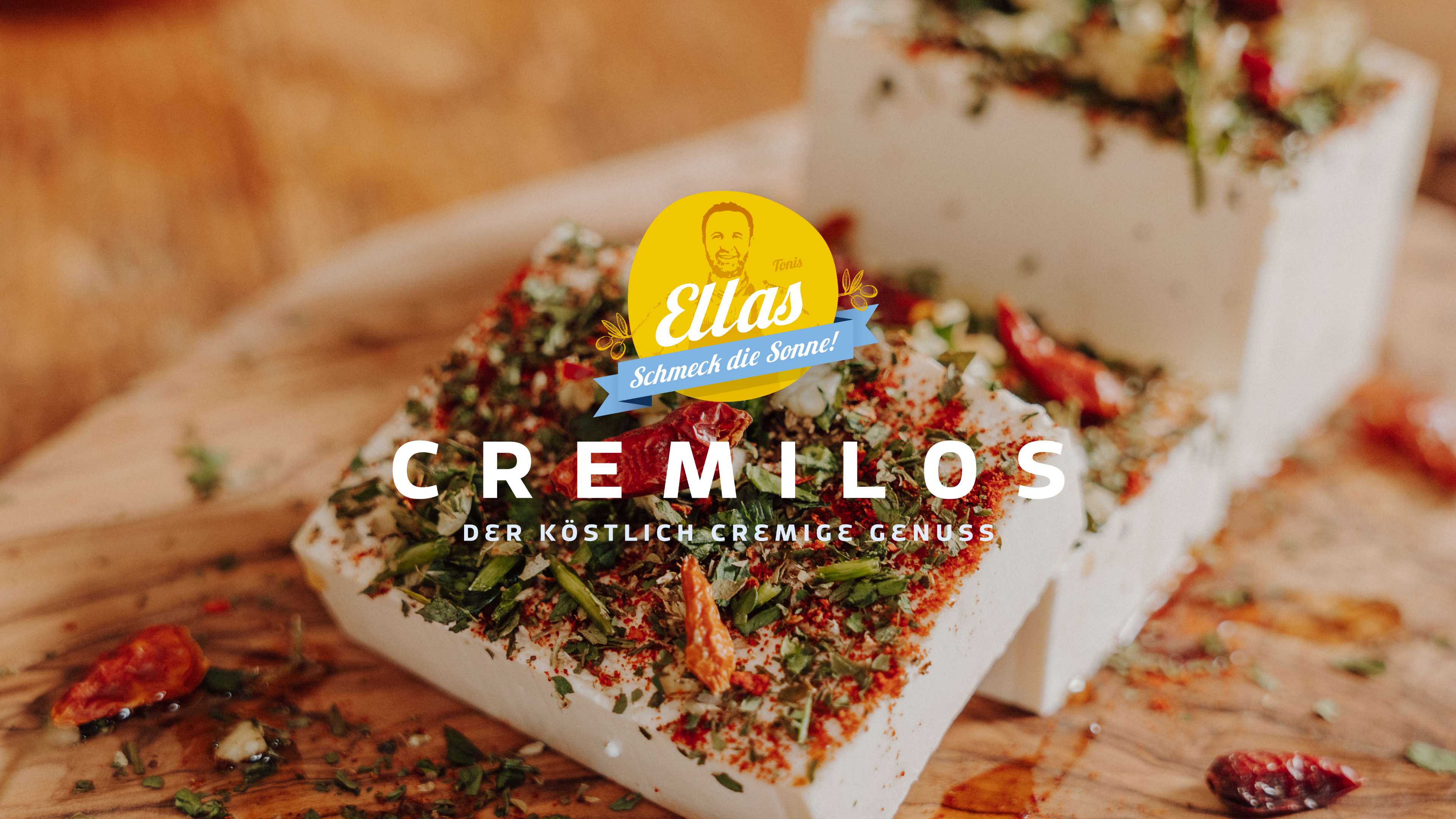 Foto mehrerer Blöcke Weichkäse mit Kräutern und Chilis drauf und dem Schriftzug Cremilos der köstlich cremige Genuss darüber das Logo von Tonis Ellas in gelb mit der Silhouette eines Mannes und dem Satz Schmeck die Sonne