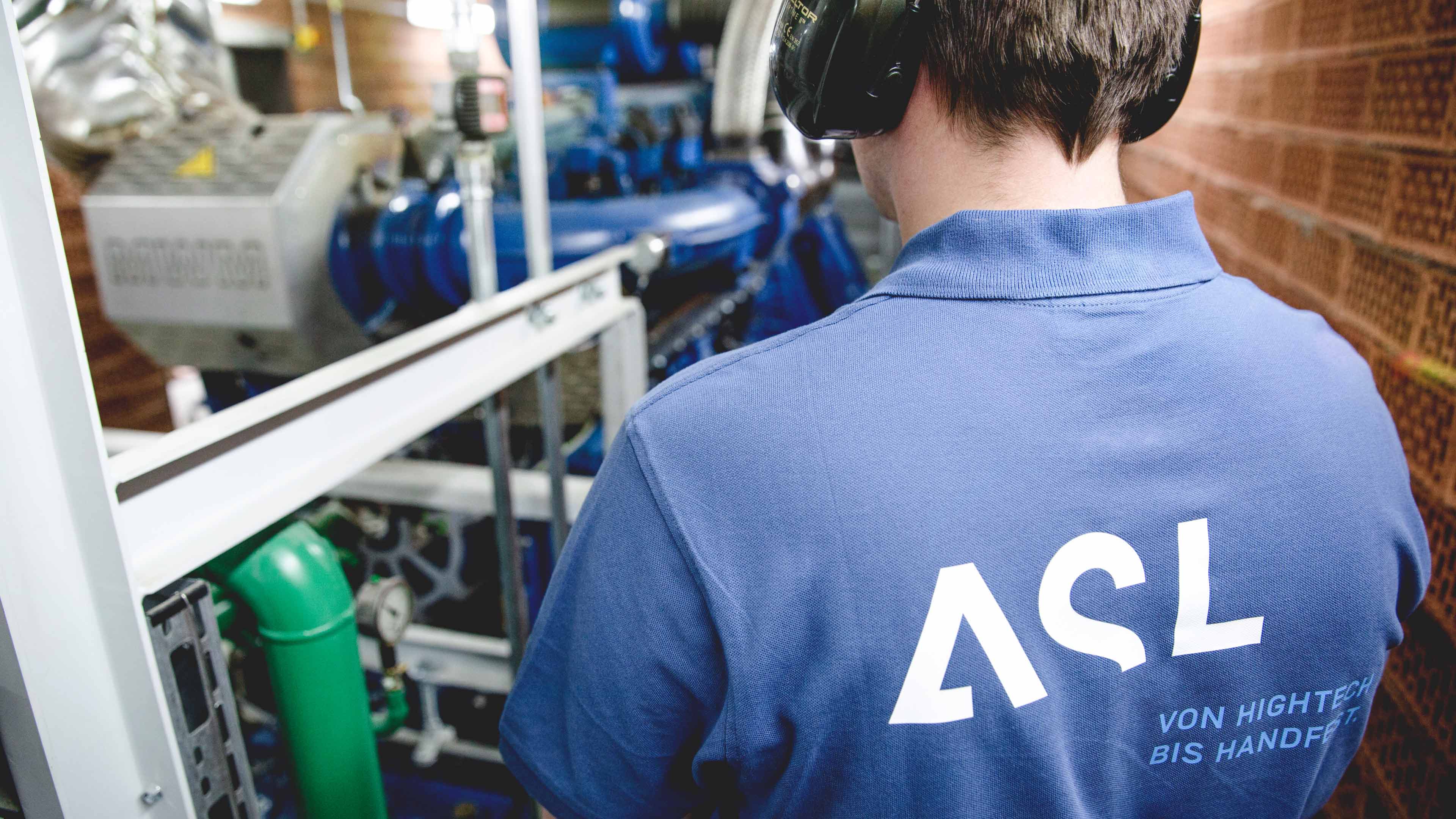 Blick auf Schulter eines Mitarbeiters im blauen ASL-Poloshirt, der mit Ohrschützern an einer Maschine steht