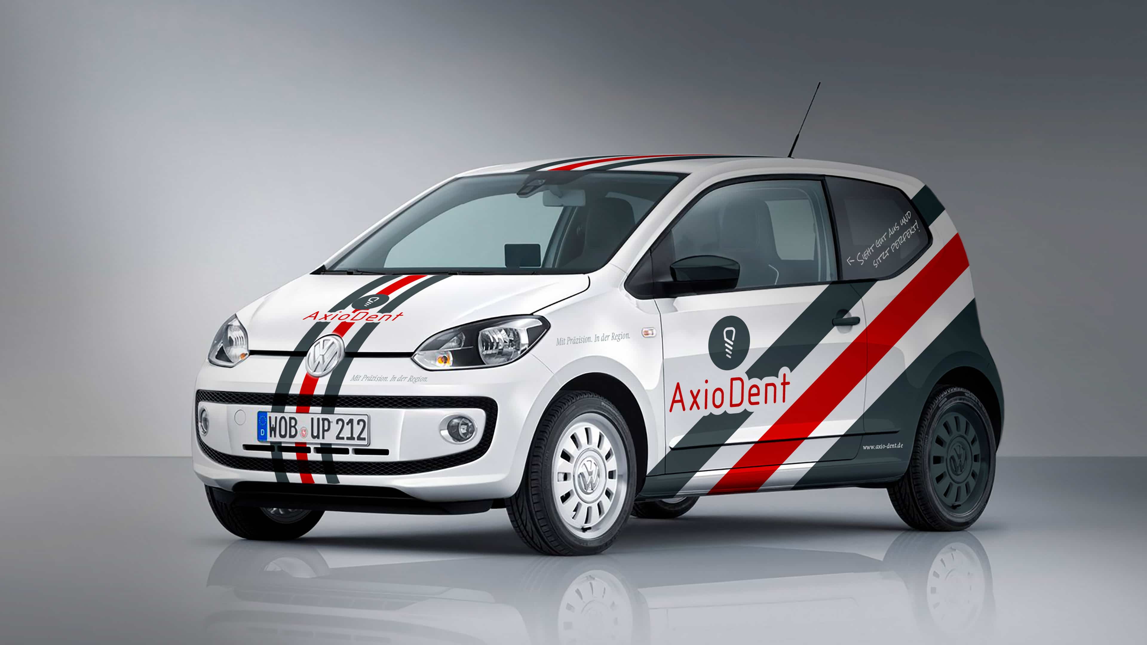Ein mit AxioDent-Logo und rot-grauen Streifen beklebter weißer VW Up von schräg vorne
