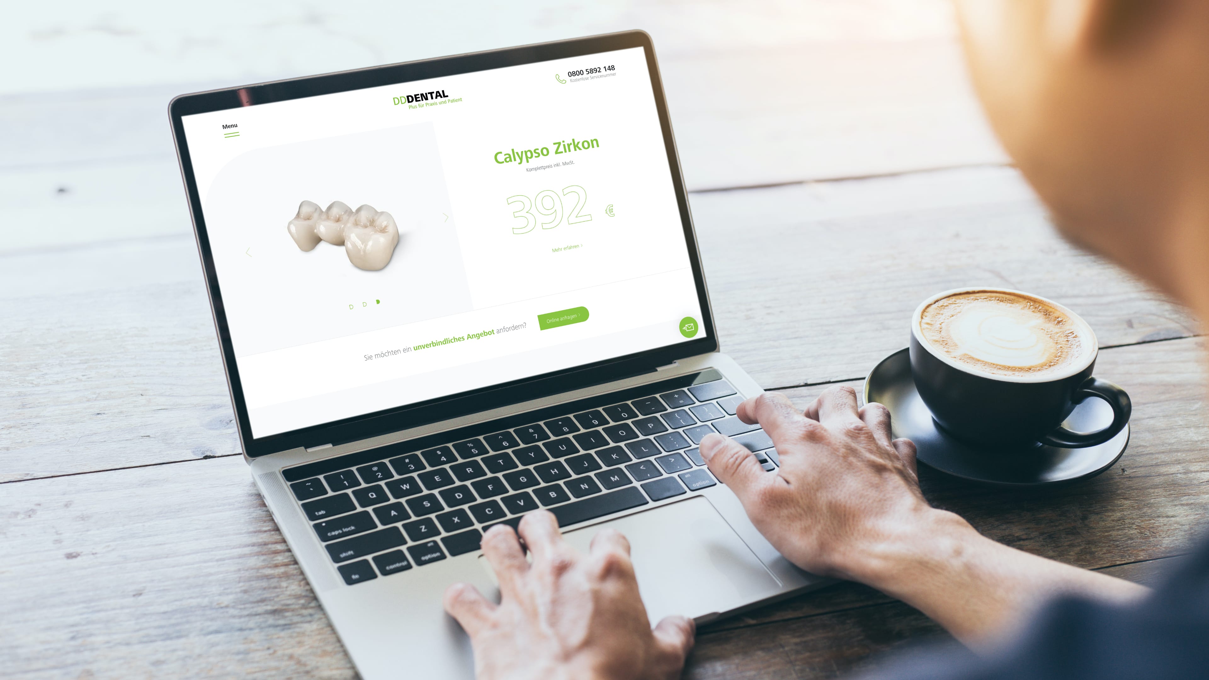 Person mit Laptop auf Holztisch, daneben ein Kaffee, zu sehen ist die weiß-grüne Website dd-dental.de