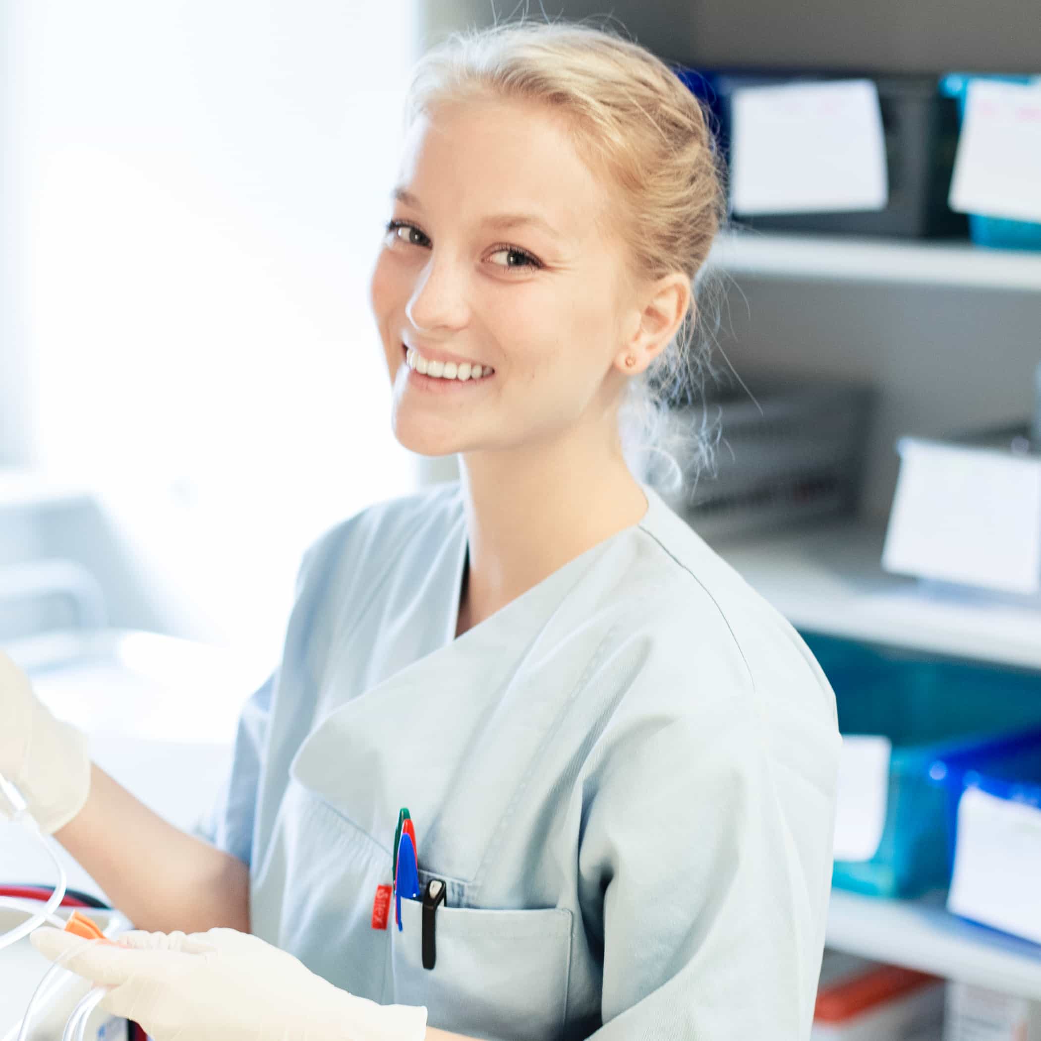 Lächelnde Blondine im Pflegehemd bei der Arbeit