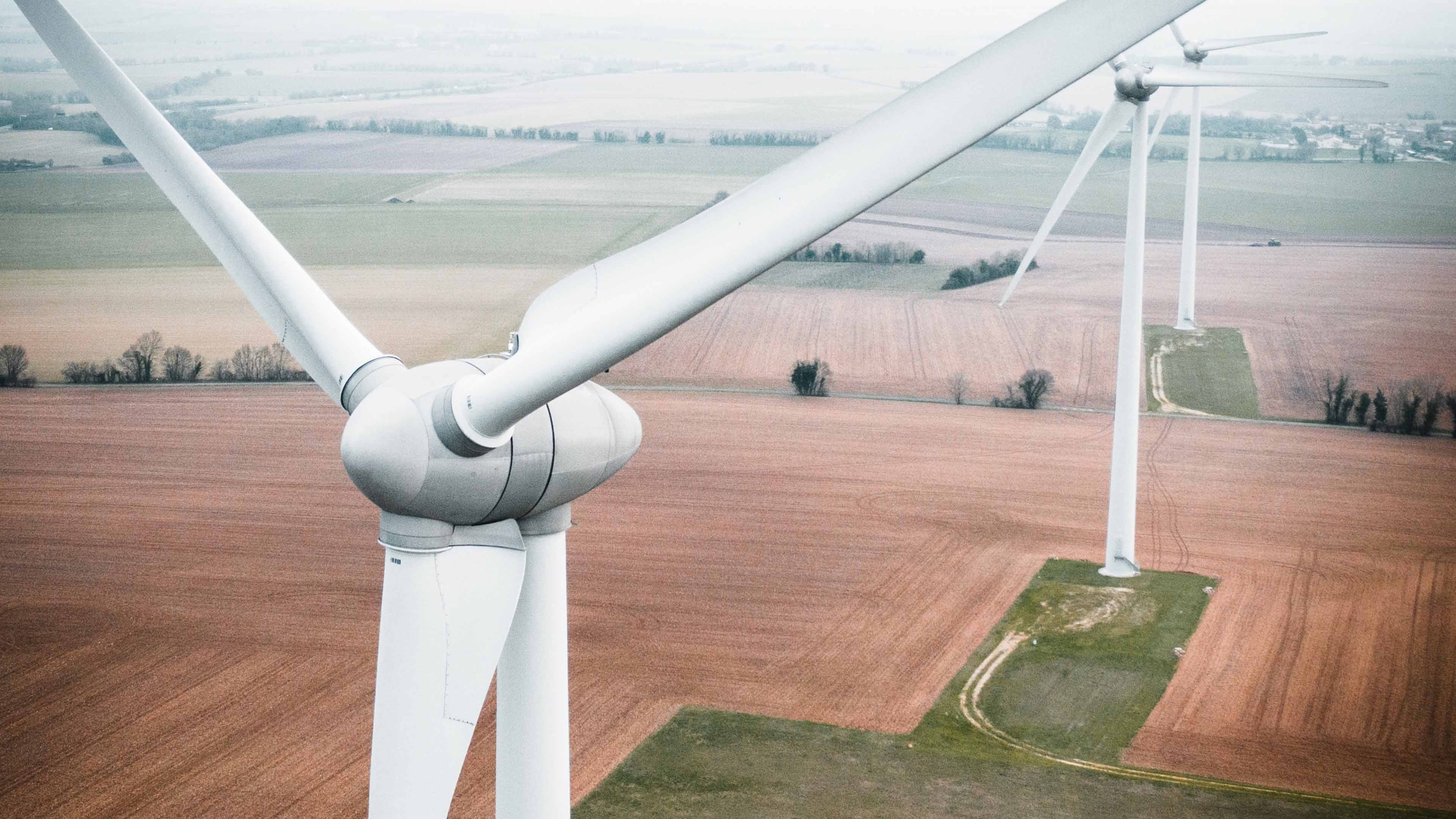 Luftaufnahme auf Höhe einer Windkraftanlage mit Blick auf drei Anlagen und Felder