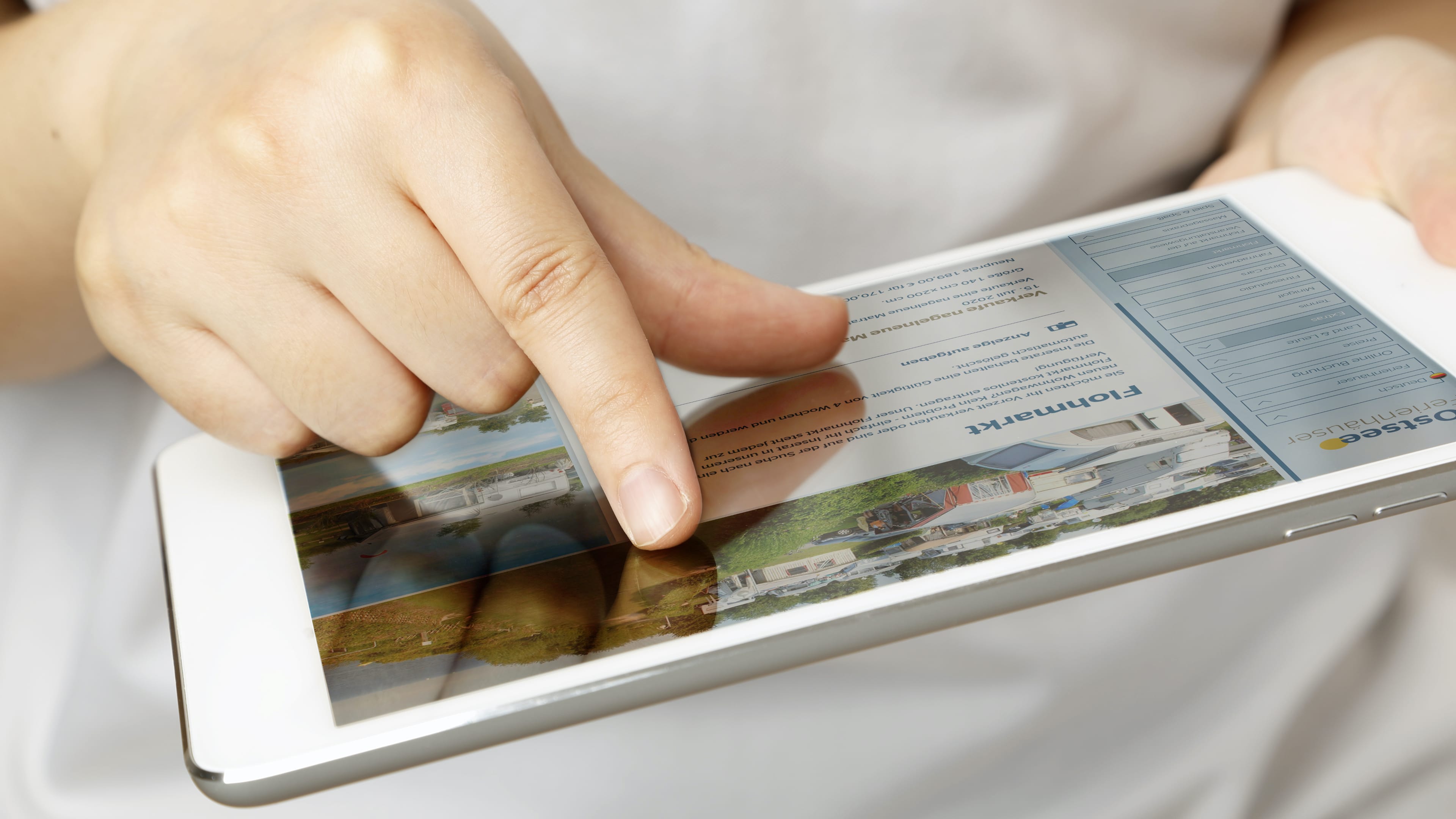 Finger auf Tablet, das die Website der Ostsee Ferienhäuser zeigt