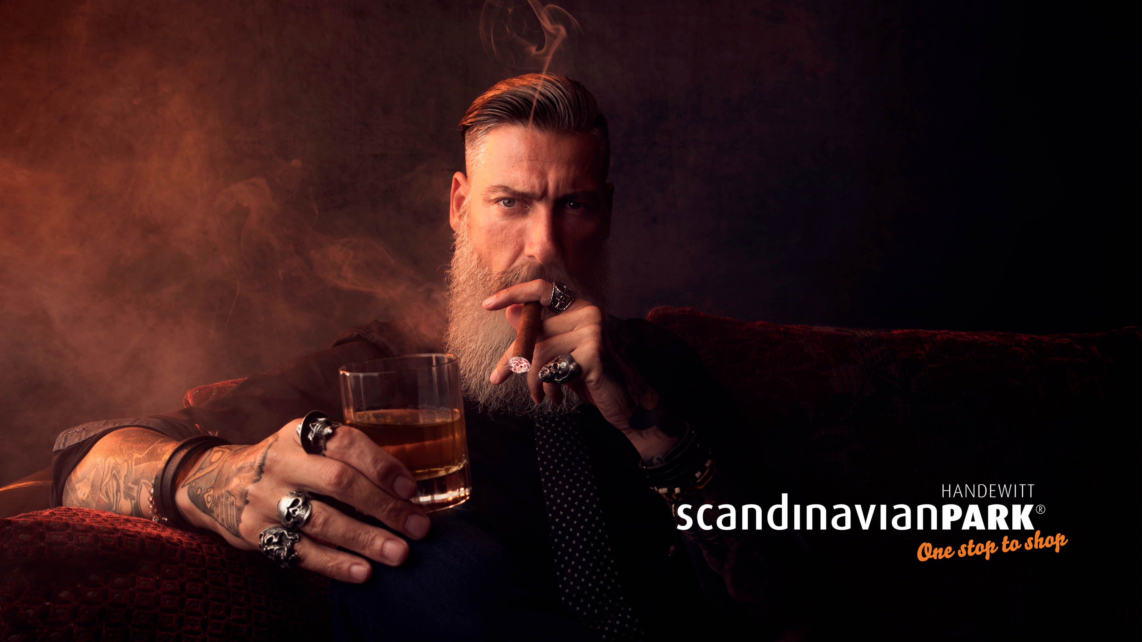 Bärtiger Mann raucht eine Cigarre und trinkt einen Whiskey