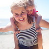 Junge Frau mit blondem Kind auf dem Rücken glücklich am Strand