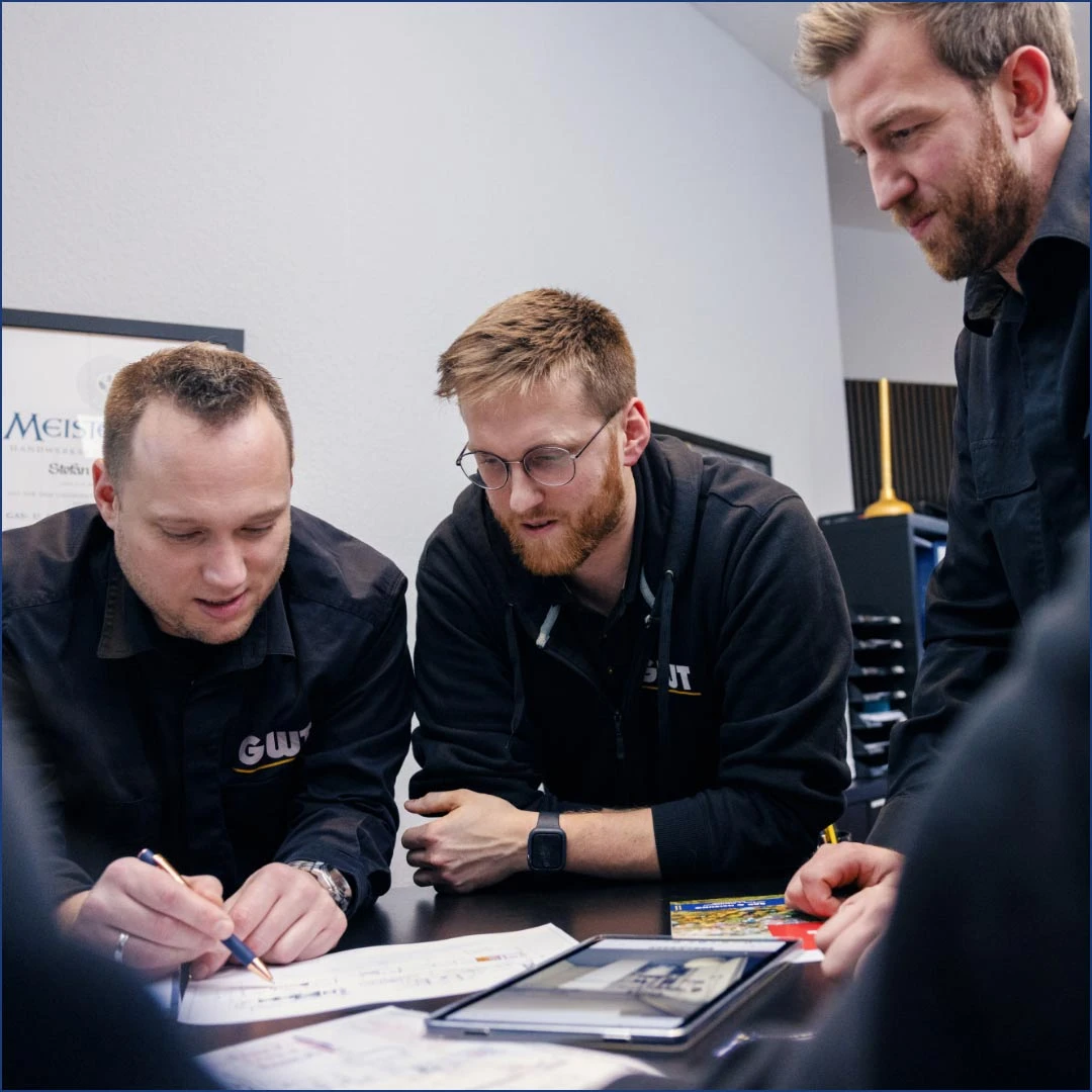 Drei Handwerker sind an einem Tisch versammelt und lesen ein Blatt Papier