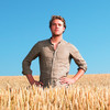 Junger Mann in braunem Leinenhemd steht in einem Kornfeld