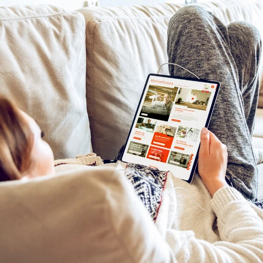 Frau liegt auf dem Sofa und schaut sich die Nospa Homepage an