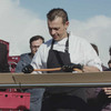 Koch mit schwarzer Schürze und Handschuhen verteilt die Wurst auf das längst Hotdog der Welt auf der Reling der Seebrücke