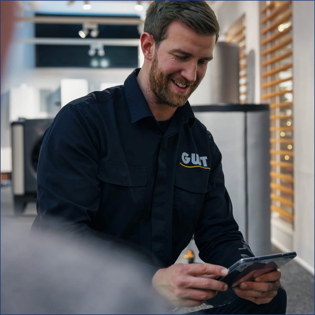 Ein schwarz gekleideter Handwerker schaut lächelnd auf ein iPad