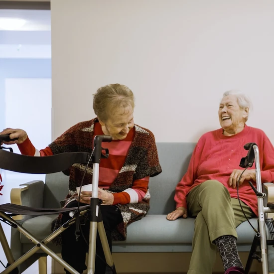 Zwei ältere Frauen sitzen auf einem Sofa und lachen zusammen