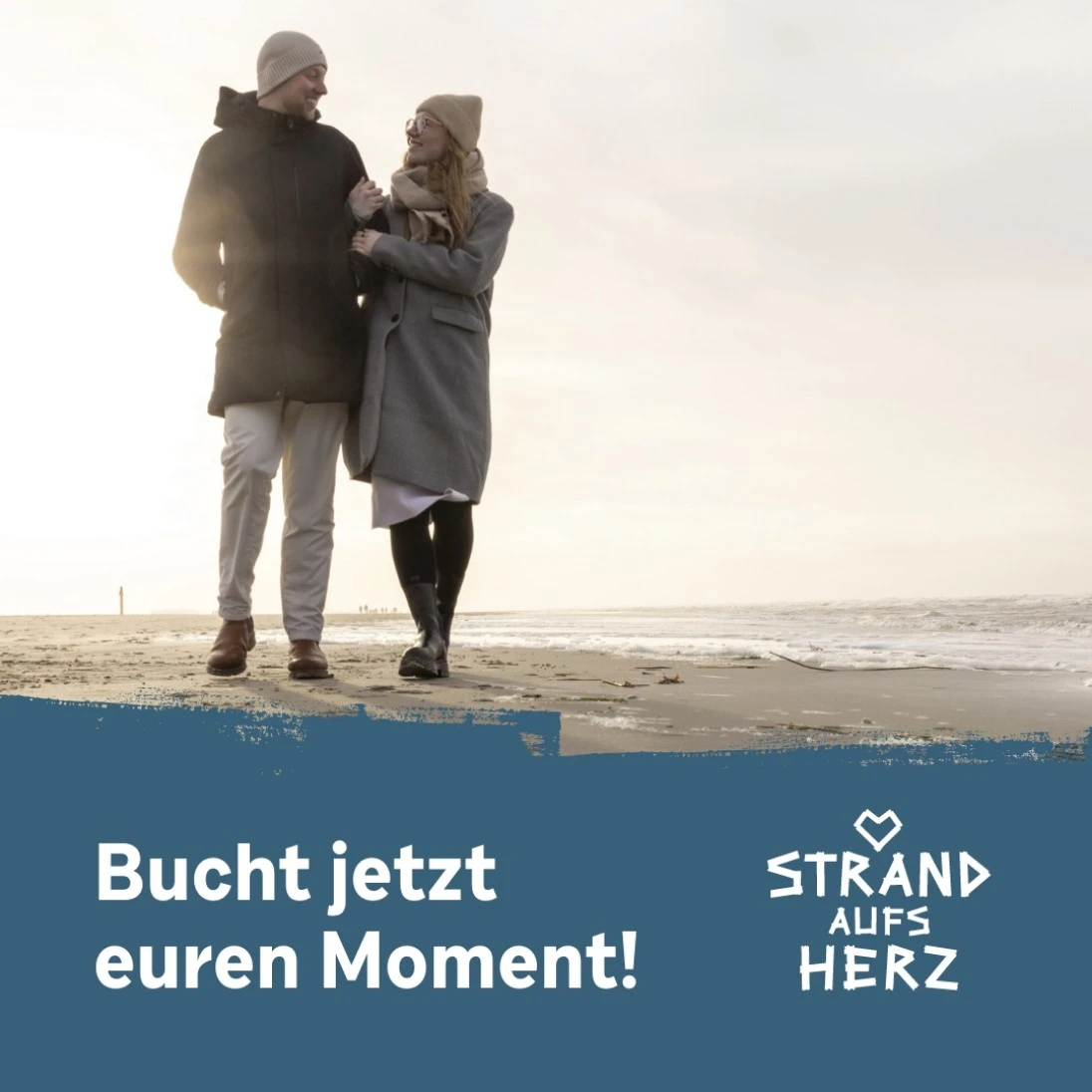 Ein Paar am Strand, darunter der Satz Bucht jetzt euren Moment und das Logo von Strand aufs Herz