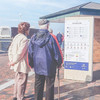 Ein älteres Ehepaar guckt sich die Infotafel der Strandstraße auf Sylt an