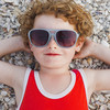 Rothaariges Kind mit Sommersprossen trägt roten Badeanzug und eine Sonnenbrille