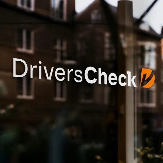 Fensterscheibe mit dem neuen DriversCheck Logo in der sich das gegenüberliegende Haus spiegelt