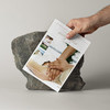 Hand hält weißes Magazin über den Alten Meierhof vor einem grauen Stein