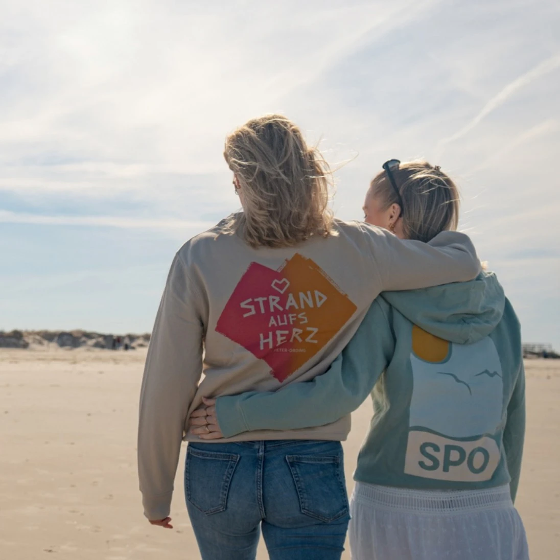 Zwei Personen von hinten fotografiert Arm in Arm am Strand