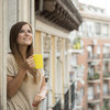 Braunhaarige Frau mit gelbem Becher schaut vom Balkon