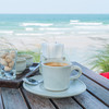 Eine Tasse mit Kaffe steht auf einem Tisch am Meer