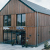 Zweistöckiger Holzbau mit bodentiefen Fenstern und einem Eingang über dem Hofküche steht