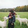Kind mit Jacke und Mütze füttert weiße Ziegen mit Apfel auf einer Wiese
