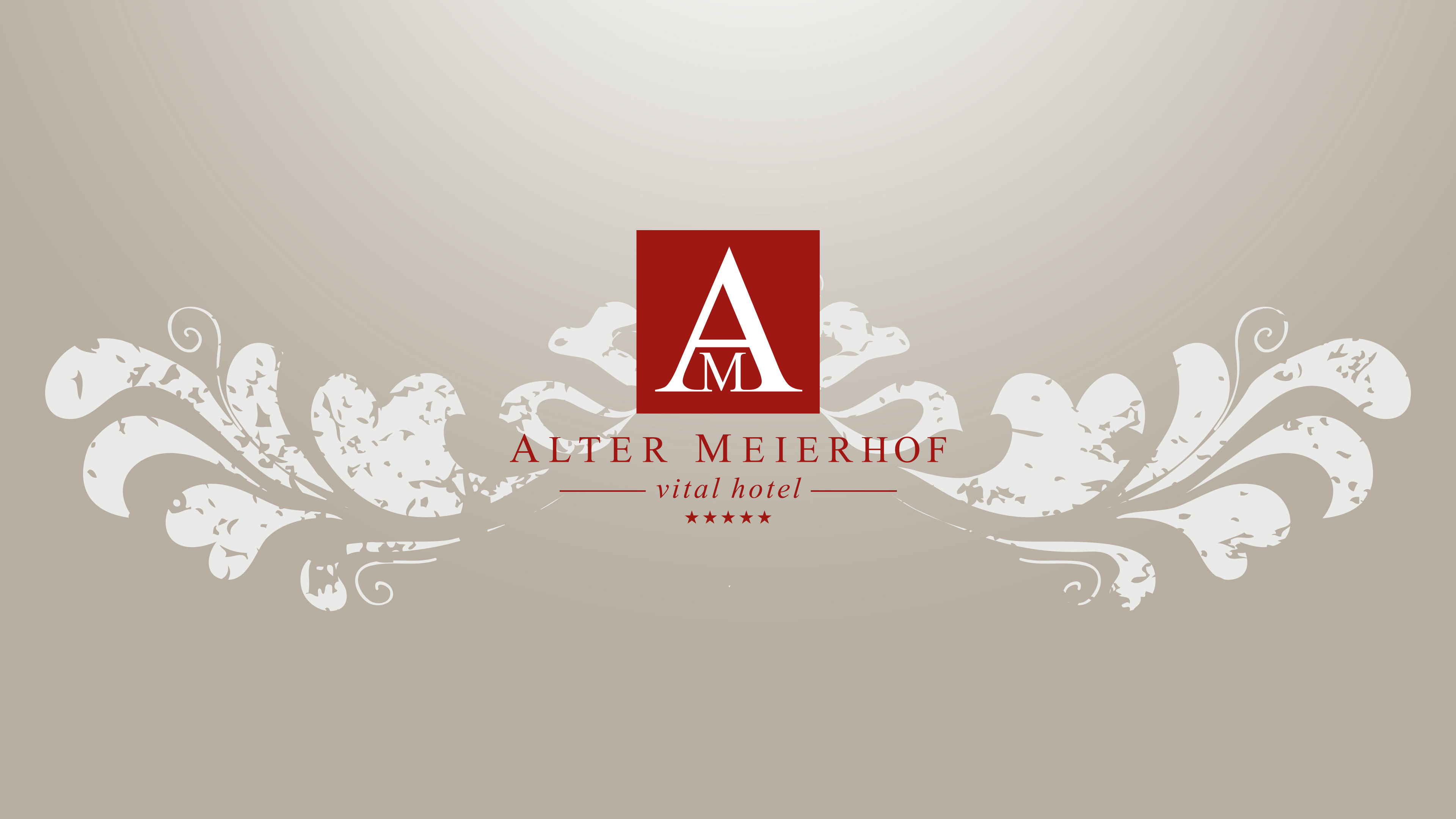 Weinrotes Logo mit großem A und kleinem M für das vitalhotel Alter Meierhof auf beigem Hintergrund mit weißem Blumenmuster