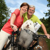 Älteres Ehepaar sitzt auf Fahrrad und hat einen Hund im Korb