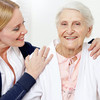 Weibliche Pflegekraft umarmt lächelnde Seniorin an den Schultern