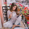 Brünette Frau sitzt auf ihrem Balkon und trinkt einen Kaffee