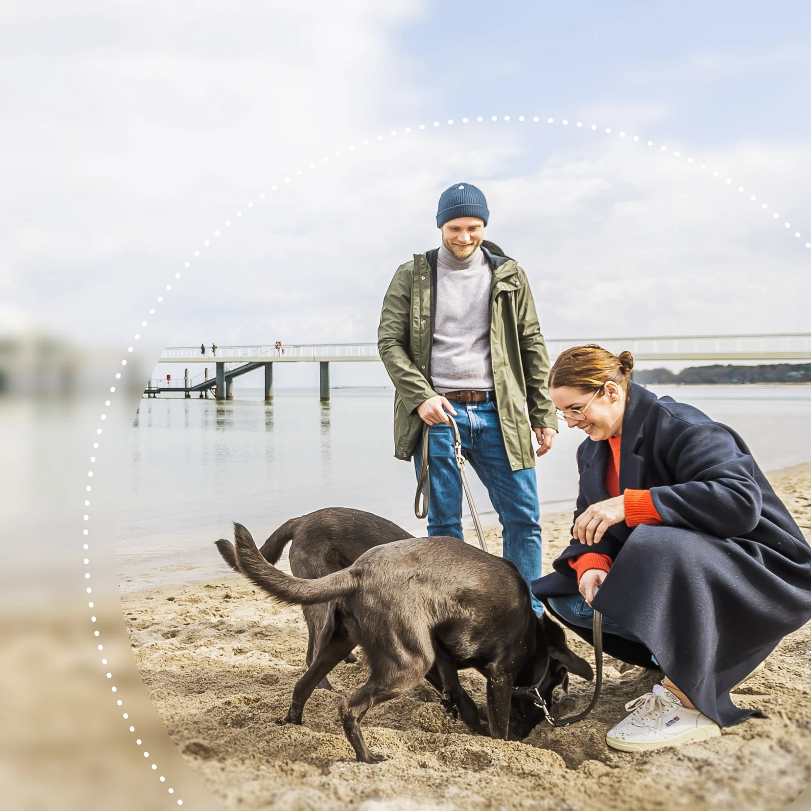Zwei Personen mit zwei Hunden am Strand