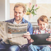 Vater und Sohn sitzen auf dem Sofa und lesen Zeitung