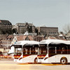 Zwei weiße Stadtbusse vor der Kulisse Flensburgs