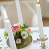 Ein rosaner Blumenstrauß umgeben von weißen Kerzen
