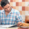 Mann im karierten Hemd sitzt am Frühstückstisch