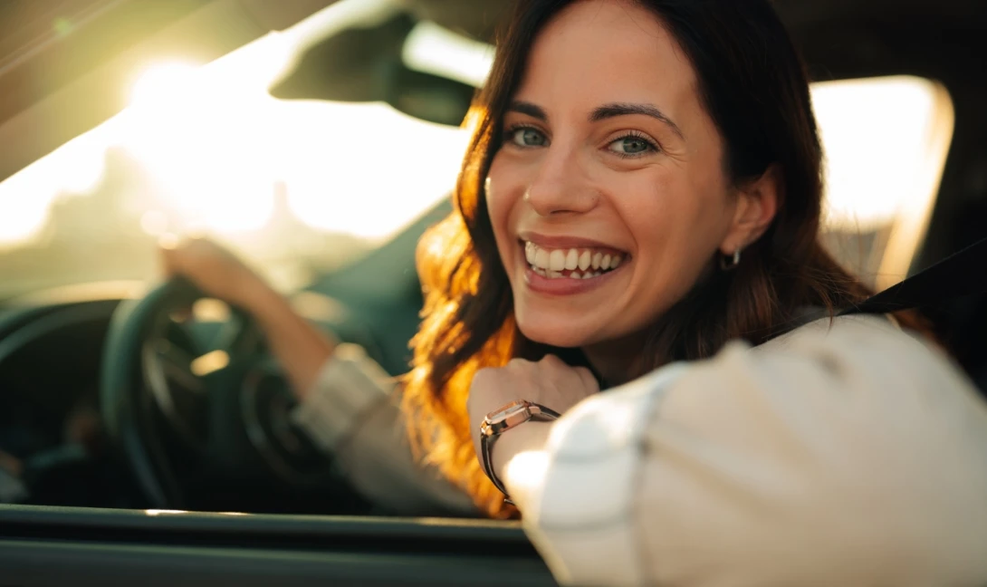 h2_driverscheck_teaser_02.jpg Eine Frau fährt ein Auto und lächelt aus dem Fenster heraus