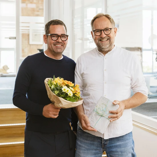 Foto von Chef Felix mit Standortleiter, Projektleiter und Prokurist Björn mit Blumen und einem Geschenk in den Händen