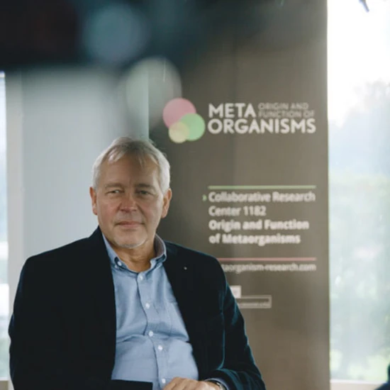 Ein älterer Herr sitzt vor einer Tafel mit der Überschrift Meta Organismus