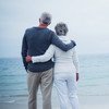 Mann und Frau fortgeschrittenen Alters stehen Arm in Arm vor dem Meer