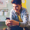 Junger Teenager hält lächelnd sein Handy in der Hand