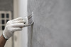 Ein Mann trägt einen weißen Handschuh während er eine Wand mit einem Pinsel grau streicht